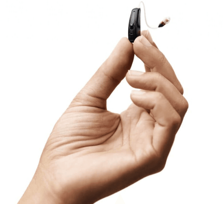 Close-up of a person's hand holding a hearing aid, flipping it over to reveal the small speaker and microphone. This hearing aid can help improve your hearing and quality of life.